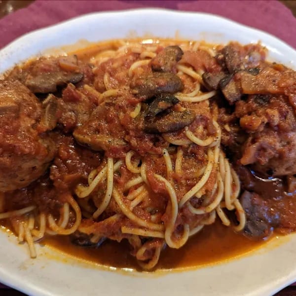 Pietros' spaghetti with meatballs and mushrooms in a rich red sauce on a white plate.