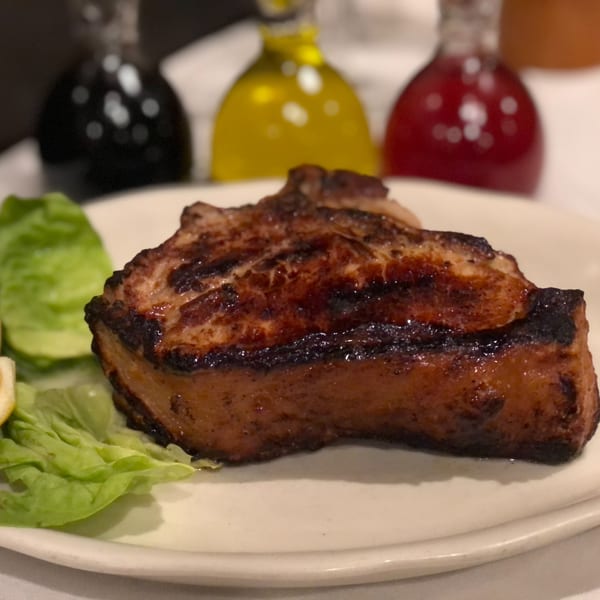 Grilled pork chop with lettuce and lemon, with oil and vinegar bottles in the background.