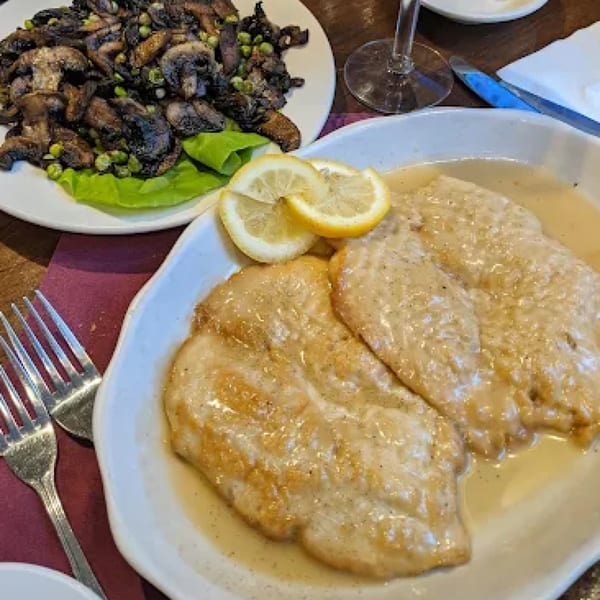 Pietros' Italian chicken in a creamy sauce with lemon slices, alongside a plate of sautéed mushrooms and peas.