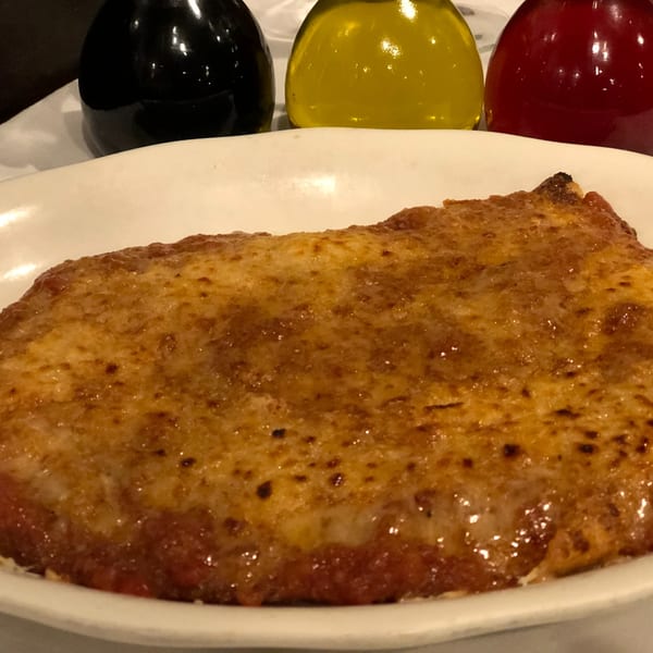 Baked Italian dish, possibly lasagna or baked ziti, with melted cheese on a white plate.