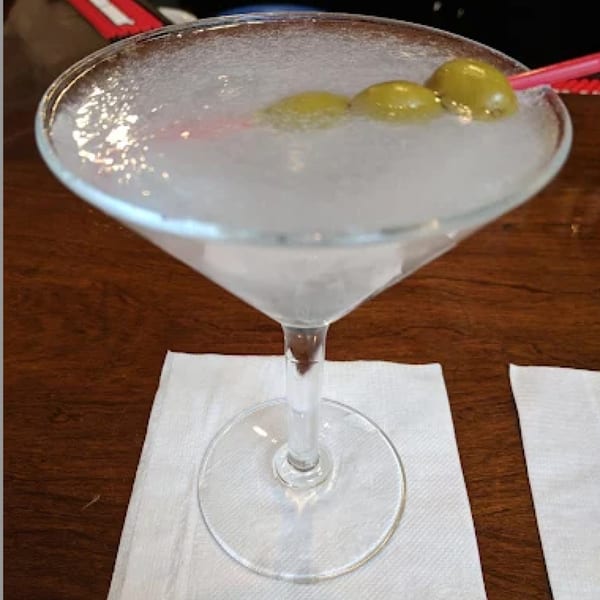 A frosty martini with three green olives and a red stirrer, on a white napkin at Pietros.