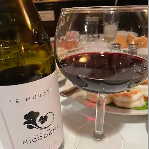 A bottle of Nicodemi red wine next to a glass filled with red wine at Pietros.